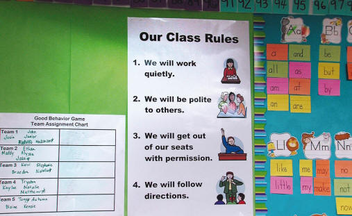 Good Behavior Game rules displayed on the classroom wall and to the left a poster with names of children assigned to each team